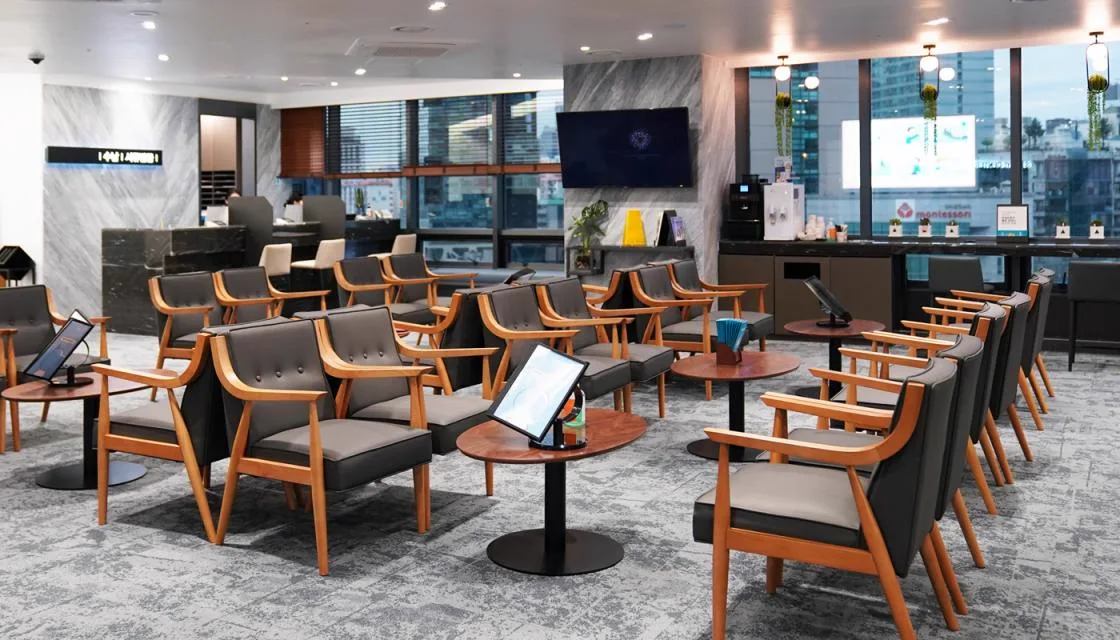8F waiting lounge with rows of wooden armchairs, side tables and a coffee station